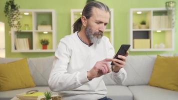 el de edad mediana hombre mirando a el teléfono es trastornado y llorando en el cara de qué él ve en el pantalla. de edad mediana hombre llanto, entristecido cuando él ve angustioso Noticias o mensaje en el teléfono. video