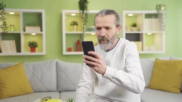 gammal man ser på smartphone på Hem gläds, vinner, glädje av Bra Nyheter. gammal man ser på hans smartphone gläds på de Bra Nyheter på Hem, gläds i hans förtjänst, tjänar i de stock marknadsföra. video