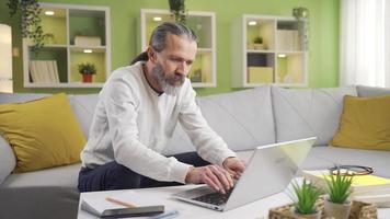 Positive mature man working at home working on laptop and dancing happily. Attractive and funny mature man working from laptop at home. video