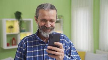 velho homem usando Smartphone rindo às engraçado videos ou mensagens. velho homem às casa tendo Diversão e alegre Tempo em dele telefone. social meios de comunicação, namoro sites.