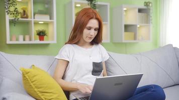 joven mujer sentado a hogar haciendo negocio en ordenador portátil. hermosa mujer sentado a hogar, felizmente haciendo su trabajo en ordenador portátil. video