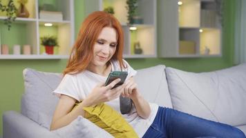 Young woman sitting at home dancing and looking at her phone. Beautiful woman sitting at home dancing happily and looking at her phone. video