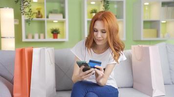 Happy young woman who loves shopping. Young woman at home with shopping bags spends on the phone with a credit card from online shopping sites. video