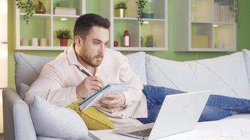 Faculdade aluna fazendo dever de casa usando computador portátil às lar. Faculdade aluna deitado em sofá fazendo dever de casa pensativamente usando computador portátil. video