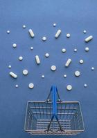 Shopping cart with medicine pills in pack on classic blue background with copy space. Creative idea for drugstore, online pharmacy, health lifestyle and pharmaceutical company business concept.