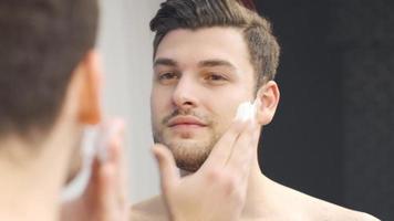 bello uomo l'applicazione rasatura schiuma per il suo barba per radersi. giovane uomo l'applicazione rasatura schiuma per il suo viso per tagliare il suo barba. video