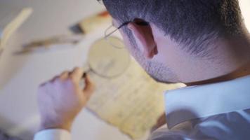 The epigraphist is examining the ancient letter and trying to translate it. Inscription scientist young man examines and researches historical literature texts with a magnifying glass. video