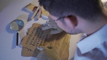 das Epigraph ist Prüfung das alt Brief und versuchen zu Übersetzen Es. Inschrift Wissenschaftler jung Mann untersucht und forscht historisch literarisch Texte, Kommunikation Texte mit ein Vergrößerung Glas. video