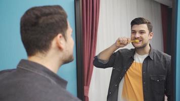 Jeune homme brossage le sien les dents dans de face de le miroir. personnel se soucier. Beau Jeune homme brossage le sien les dents à la recherche à lui-même dans le miroir, aime blanc dents, jouit personnel se soucier. video