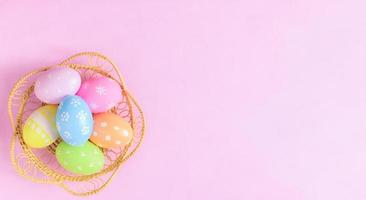 Happy Easter holiday greeting card concept. Colorful Easter Eggs and spring flowers on pastel pink background. Flat lay, top view, copy space. photo