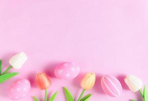 Happy Easter holiday greeting card concept. Colorful Easter Eggs and spring flowers on pastel pink background. Flat lay, top view, copy space. photo