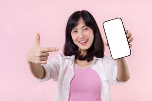 happy smiling young asian woman recommending showing new application or mobile advertisement, mockup smartphone template banner isolated on pink background. Collage blank screen digital mobile device. photo