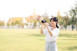 Portrait of asian woman traveler using camera. Asia summer tourism vacation concept with the grand palace in a background at Bangkok, Thailand