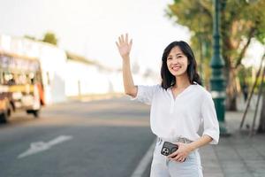 retrato joven hermosa asiático mujer ondulación mano a amigo por el calle en soleado día festivo. foto