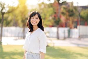 retrato joven hermosa asiático mujer con contento sonrisa alrededor al aire libre parque en soleado verano día