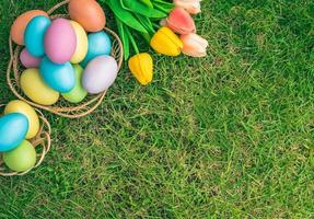 Happy Easter holiday greeting card concept. Colorful Easter Eggs and spring flowers on green grasses background. Flat lay, top view, copy space. photo