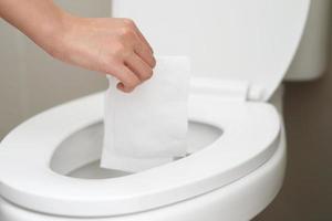 close up hand holding a tissue to be thrown into the toilet bowl. Can not drain water of toilet paper in the toilet bowl cause the stool to clog up. photo