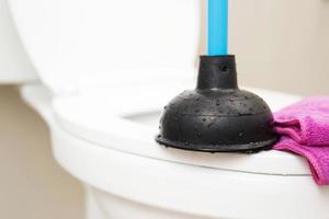 A serviceman is repairing a toilet with a hand plunger caused by a clogged toilet. photo