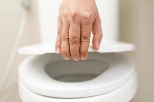 cerca arriba mano de un mujer clausura el tapa de un baño asiento. higiene y salud cuidado concepto. foto