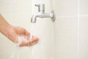 masculino mano pruebas grifo fuerza desde grifo agua en baño foto