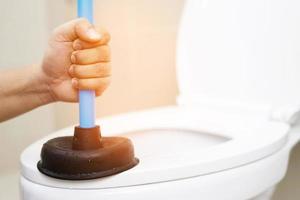 Serviceman repairing toilet with hand plunger. Clogged toilet. photo