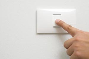 apague la luz, cierre la mano del hombre del dedo está cerrando el interruptor de encendido con la pared en casa para ahorrar energía. reducir el calentamiento global. foto