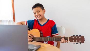 The story of a boy watching a notebook computer while preparing to practice playing guitar at home. Boys take classical guitar lessons online. photo