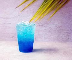 bebida hawaiana azul en un vaso de plástico y hojas de coco. foto