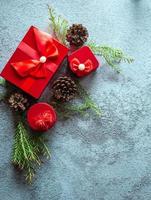 Christmas decoration composition on gray concrete background with a beautiful Red gift box with red ribbon, tree branches, and pine cones photo