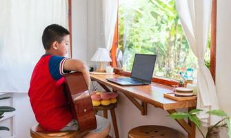 The story of a boy watching a notebook computer while preparing to practice playing guitar at home. Boys take classical guitar lessons online. photo