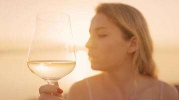 bellissimo donna Tenere un' vino bicchiere contro un' scintillante mare e cielo a tramonto video