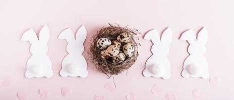 Web banner happy easter white rabbits, nest with eggs and hearts on pink background top view photo