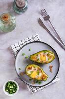 Egg baked in avocado sprinkled with bacon and herbs on a plate top and vertical view photo
