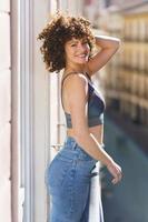 Positive young woman smiling and touching hair on balcony photo