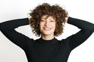 contento mujer con Rizado pelo sonriente con manos detrás foto