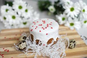 Easter cake with white icing stands on a board with quail eggs and white flowers photo