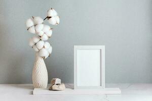 Eco friendly home decor cotton branch in a vase, photo frame and stones on the table on a gray background. Pastel shades