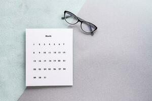 blanco sábana de mensual calendario y lentes en un texturizado antecedentes. hora planificación y organización. Copiar espacio foto