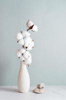 Eco friendly home decor cotton branch in vase and stones on table on gray background. Vertical view photo