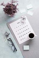 blanco sábana de mensual calendario, anteojos, café taza y alarma reloj en el escritorio. hora planificación y organización. vertical ver foto