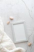 Eco friendly home template blank photo frame, knitted sweater and stones on gray background. Pastel shades. Vertical view