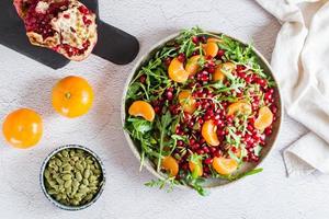 Fruit vitamin salad of pomegranate, tangerine, arugula and pumpkin seeds in a plate on the table. Organic vegetarian food.  Top view photo