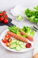 Ready-to-eat fried sausages and fresh vegetables on a plate on the table. Hearty homemade snack. Vertical view photo