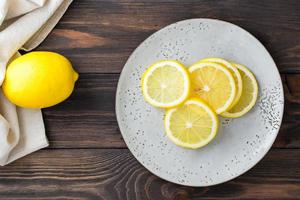 Sliced round pieces of lemon on a plate and a whole lemon next to it on a wooden table. Organic nutrition, source of vitamins. Top view photo