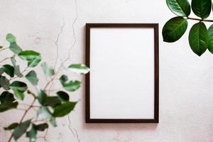 Eco mock up. Empty frame with a blank sheet on a light concrete background and leaves of home plants. Top view. photo