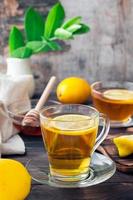 A cup of tea with a slice of lemon and a bowl of honey on a wooden table. Vitamin warming drink. Vertical view photo