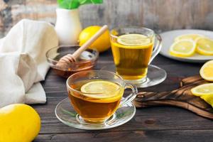 dos tazas de té con limón y un cuenco de miel en un de madera mesa. vitamina calentamiento bebida foto