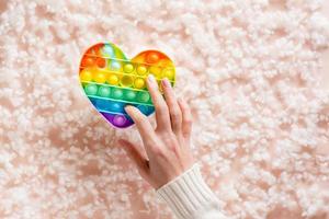 A female hand presses a silicone rainbow antistress toy on a background of fluff. A modern way to relax photo