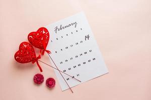 Valentine's Day. Calendar sheet with highlighted date February 14 and two hearts on sticks on a pink background. Top view photo