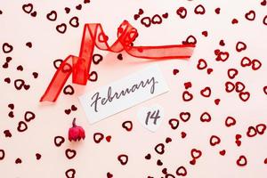 Valentine's Day. Date of February 14, dry flower and red ribbon on pink heart-strewn background photo